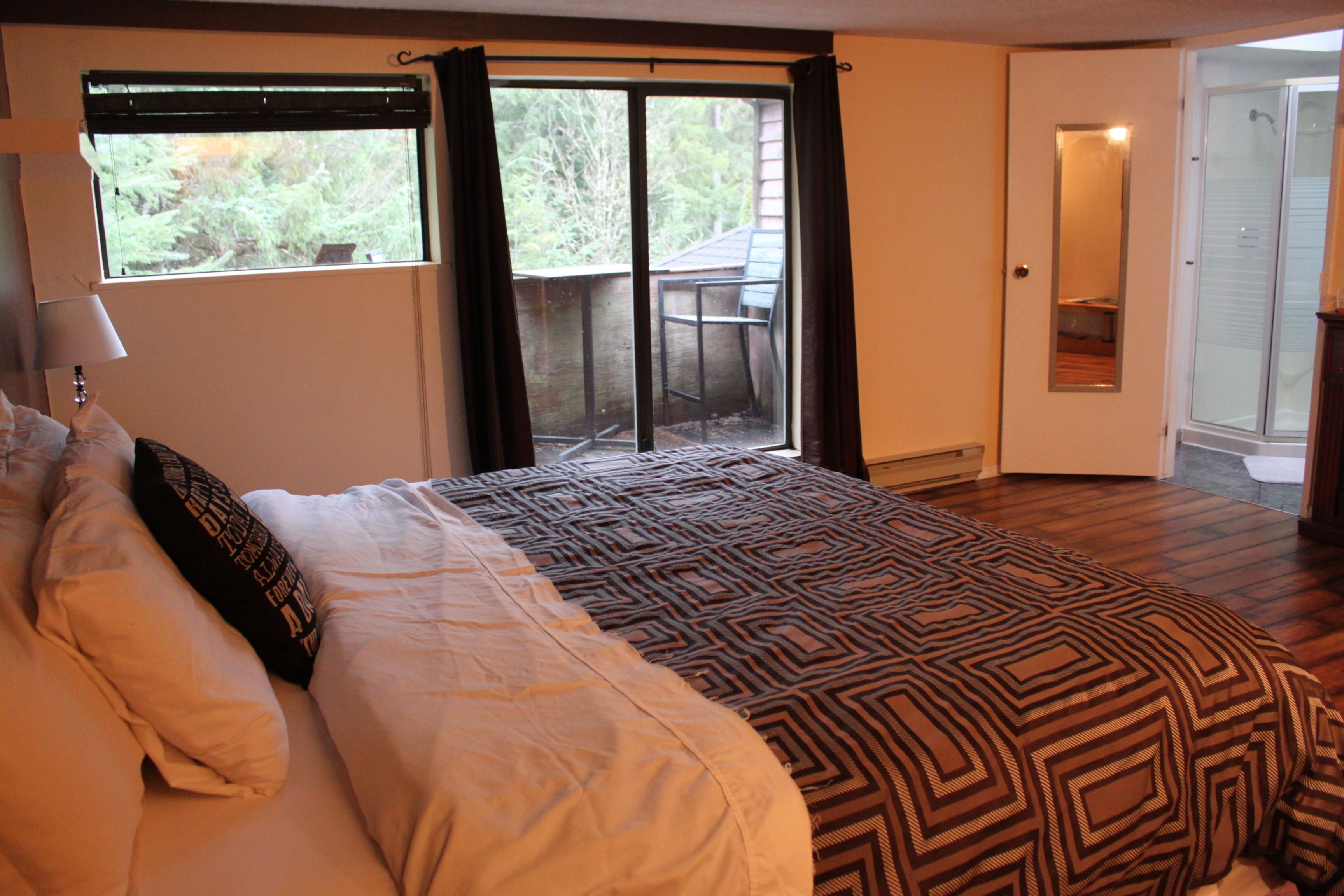 A bedroom with a large bed, a window with curtains, a door leading to a balcony, and a mirror on the wall.