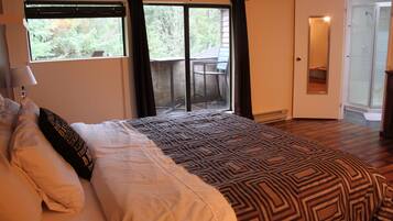 A bedroom with a large bed, a window with curtains, a door leading to a balcony, and a mirror on the wall.