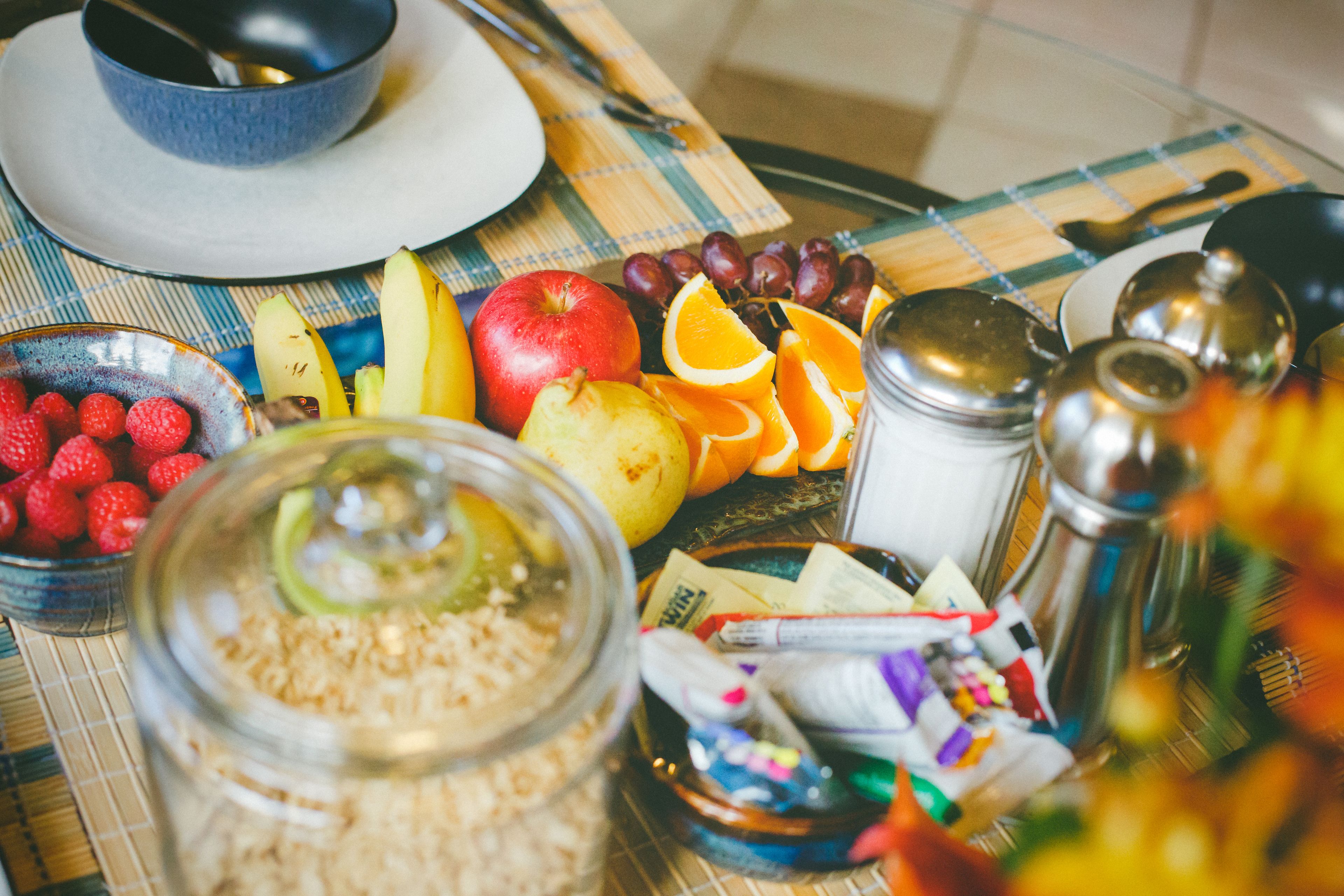 Uma mesa com diversos alimentos, incluindo frutas, uma tigela de morangos, um pote de granola e temperos.