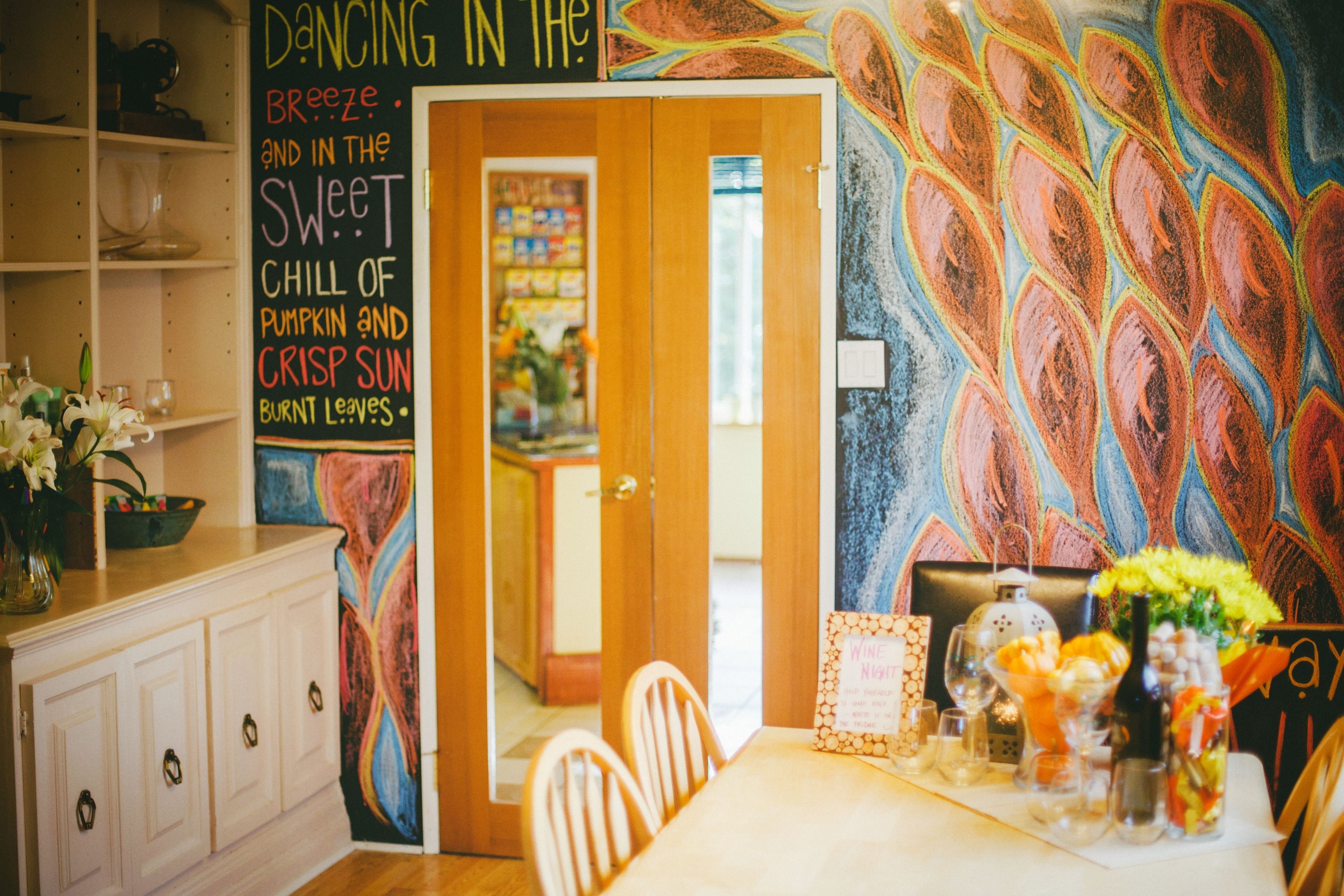 A dining area with a table set for two, a wall with colorful abstract art, and a sign with a poem.
