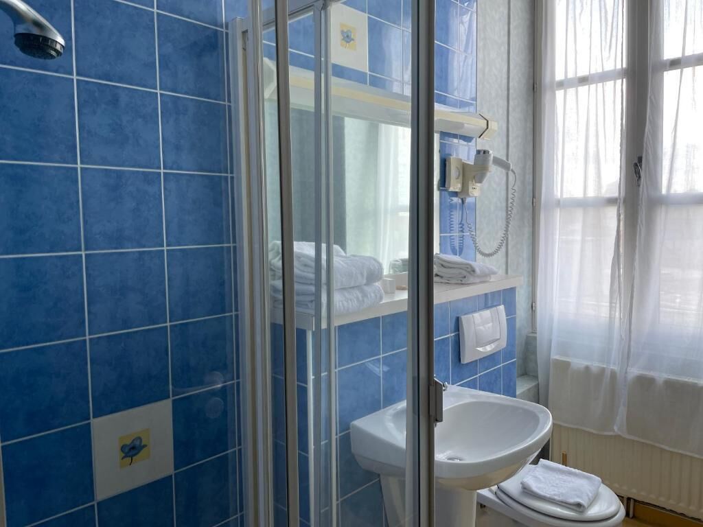 Casa de banho com azulejos azuis, cabine de duche em vidro, lavatório branco e sanita.