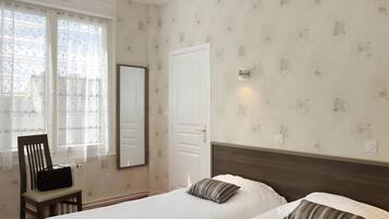 Una habitación de hotel con dos camas, una silla, un ventanal con cortinas traslúcidas y una puerta.