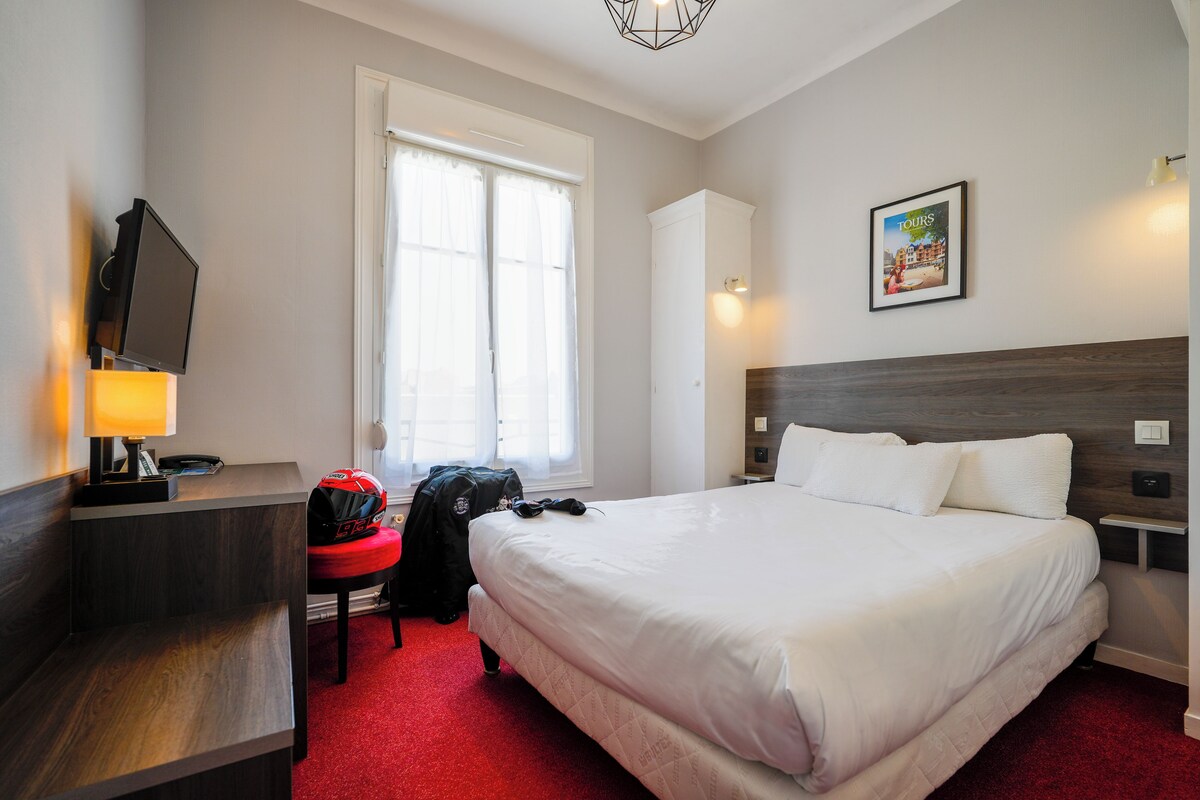 Une chambre d’hôtel avec un lit, un bureau doté d’une lampe, une chaise, une fenêtre et un tableau accroché au mur.