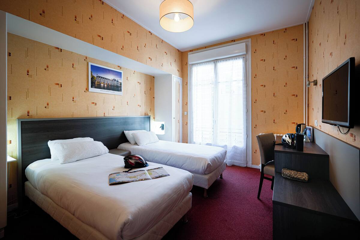 Une chambre d’hôtel avec deux lits, un bureau, une chaise, une télévision et une fenêtre avec des rideaux.