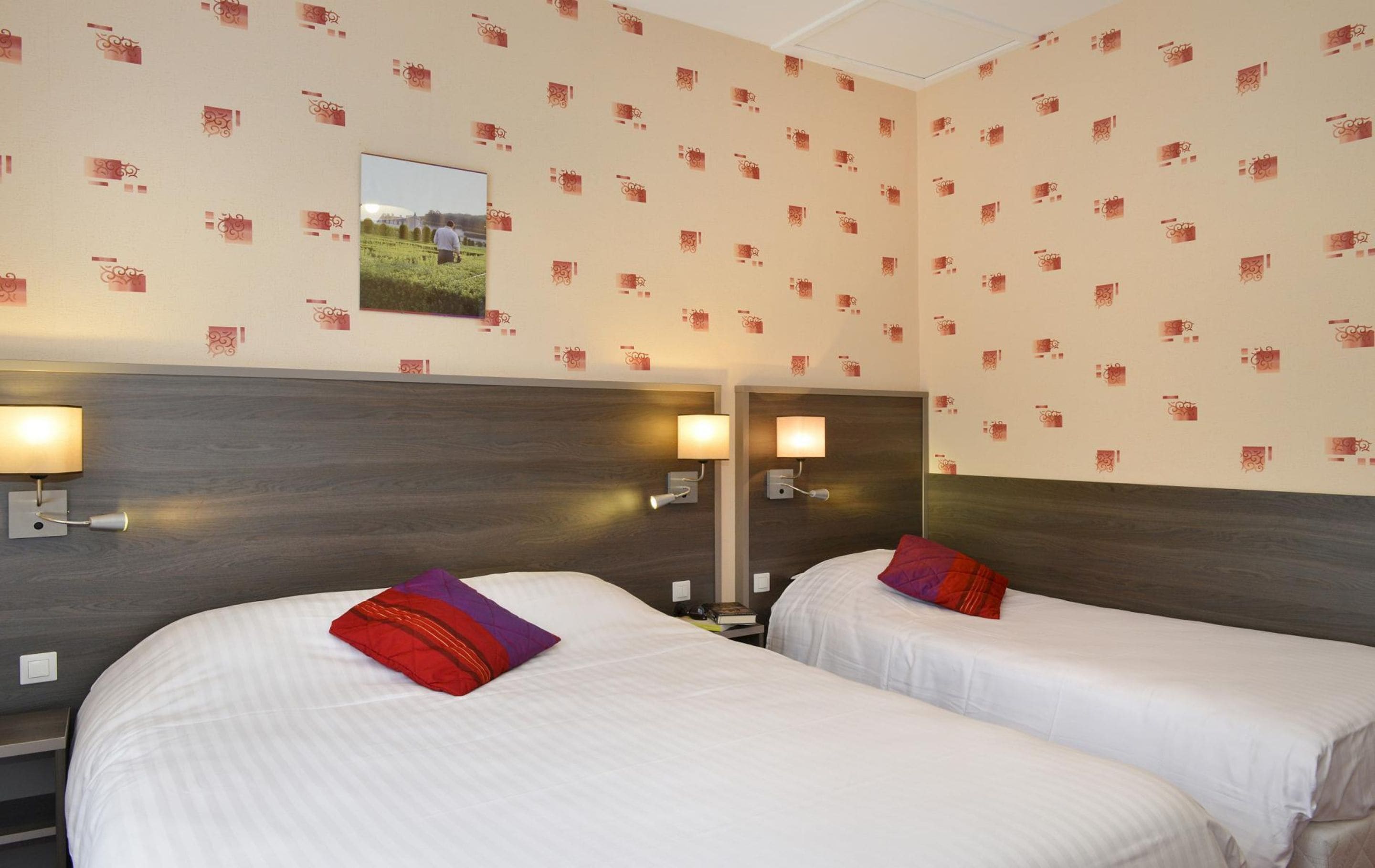 Ein Hotelzimmer mit zwei Betten, jeweils mit Kissen und einem Nachttisch. An jeder Seite der Betten befinden sich Wandleuchten.