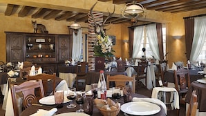 Un espace repas avec des tables et des chaises en bois, ainsi qu’un lustre. On y trouve des éléments décoratifs, comme des bois de cerf et une statue de renard.
