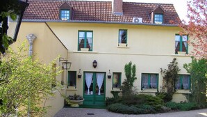 Un bâtiment à deux étages, doté d’une façade jaune, de volets verts et d’une allée gravillonnée.