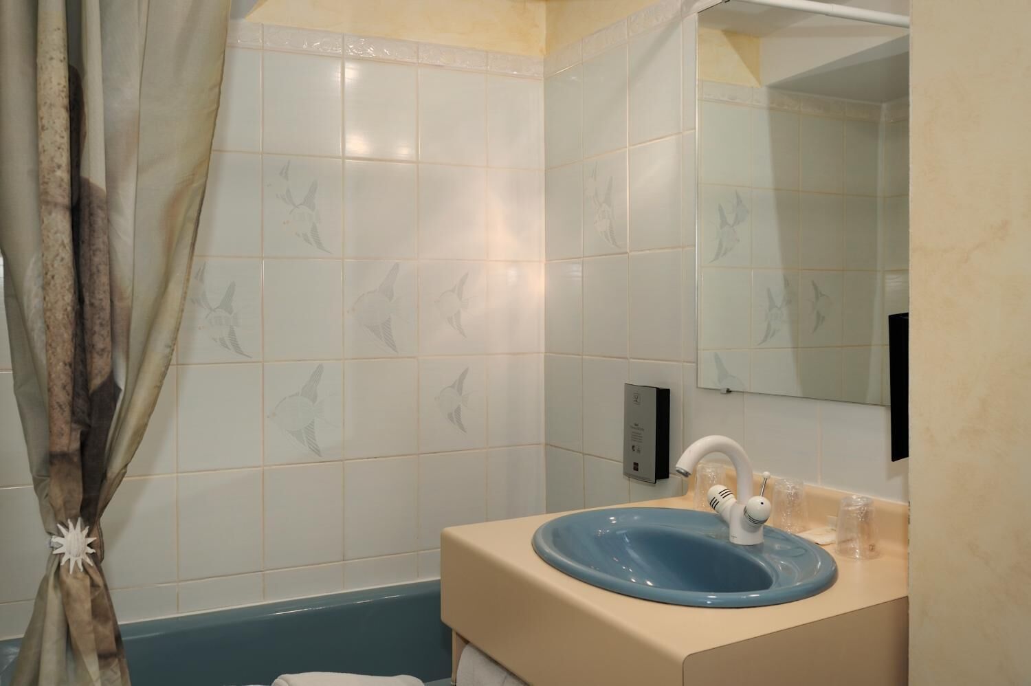 Un baño con un lavabo azul, paredes con azulejos blancos, una cortina de ducha y un espejo.