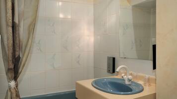 Un baño con un lavabo azul, paredes con azulejos blancos, una cortina de ducha y un espejo.