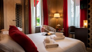 Habitació d'hotel amb llit, escriptori, cadira, làmpada i finestra amb cortines.