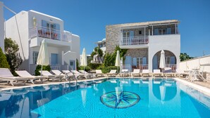 A swimming pool with lounge chairs and umbrellas, surrounded by buildings with balconies and a clear blue sky. - Hotel Katerina (Naxos)