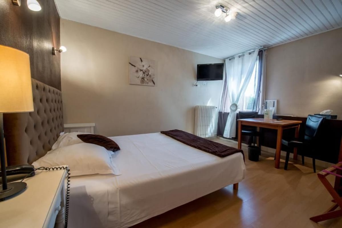 Habitación de hotel con cama, lámpara de noche, escritorio, silla y televisión en la pared.