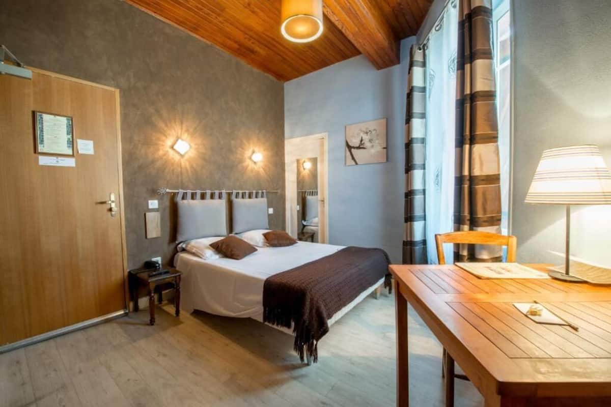 Ein Schlafzimmer mit einem Bett, Nachttischen, einer Holzbalkendecke und einem Fenster mit Vorhängen.