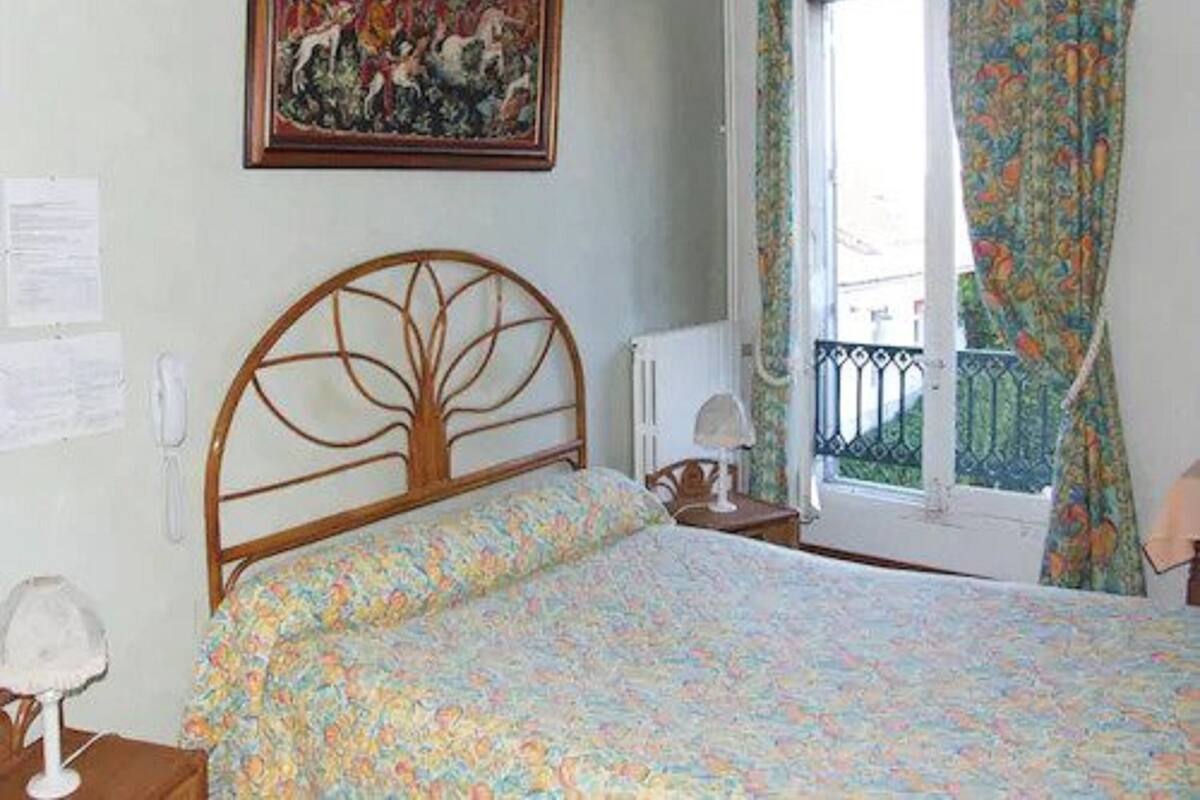 Ein Schlafzimmer mit einem Bettgestell aus Holz, floralem Bettbezug, einem Bild an der Wand und einem Fenster mit gemusterten Vorhängen.