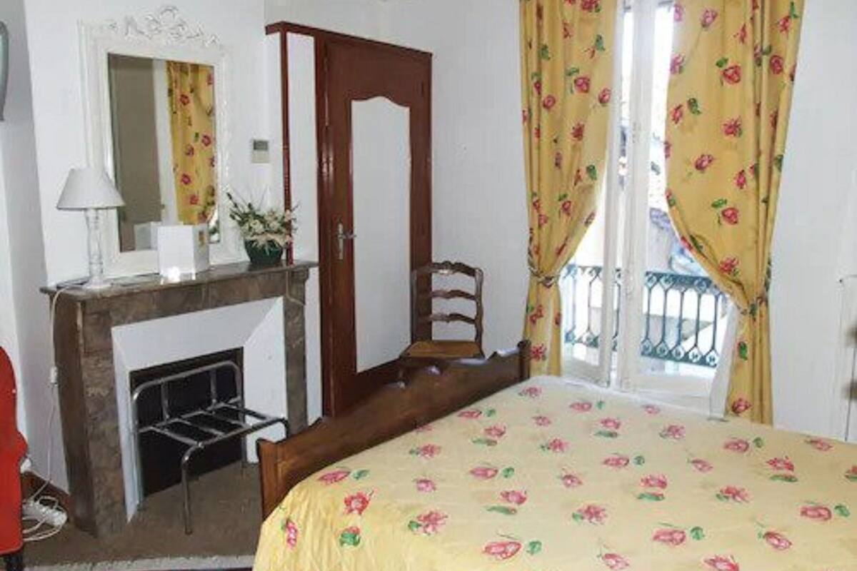 Ein Schlafzimmer mit einem Bett, einem Holzstuhl, einem Kamin, einem Spiegel und gelben Vorhängen.