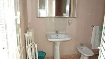A small bathroom with a pedestal sink, a bidet, a chair, and a radiator.