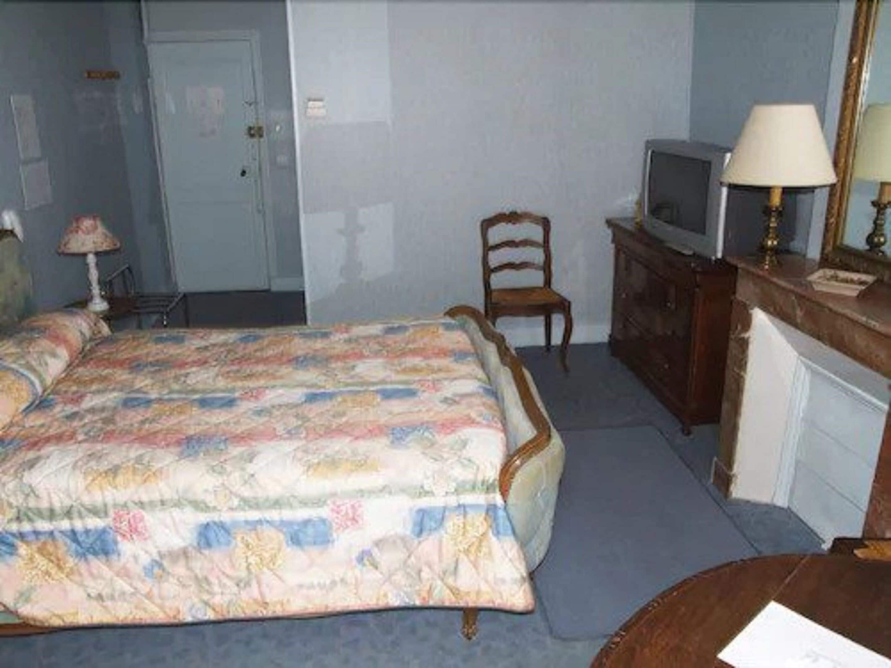 A bedroom with a bed, a chair, a dresser, a television, and a lamp.