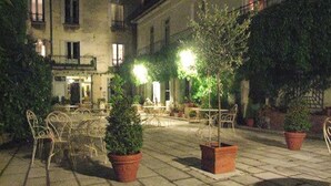 Un patio exterior con suelo de piedra, plantas en macetas y sillas de metal.