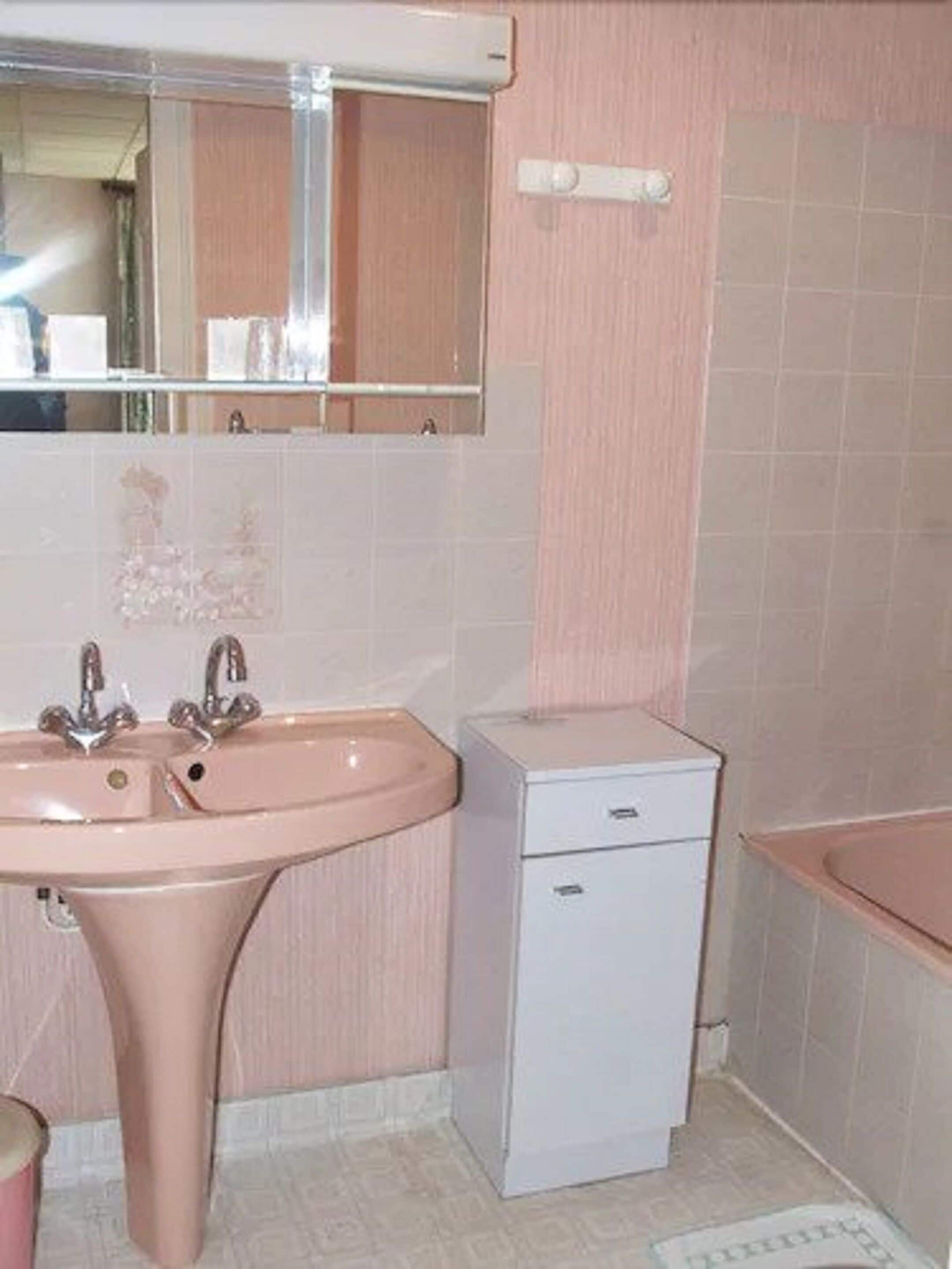 A bathroom with a pink sink, a mirror, and a small white cabinet.