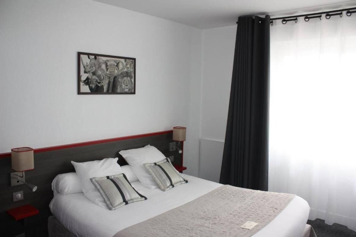 A hotel room with a bed, two bedside tables, a lamp, a picture on the wall, and a window with curtains.