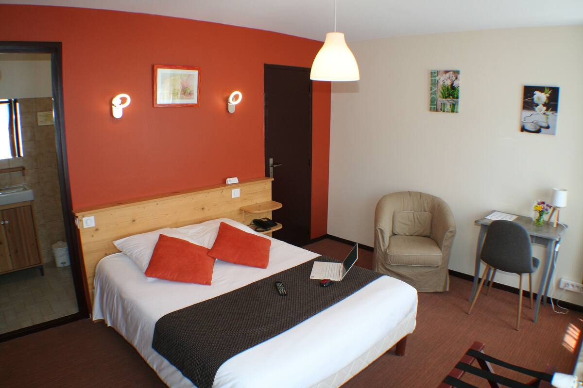 Habitación de hotel con cama, escritorio, silla y baño visible a través de una puerta abierta.