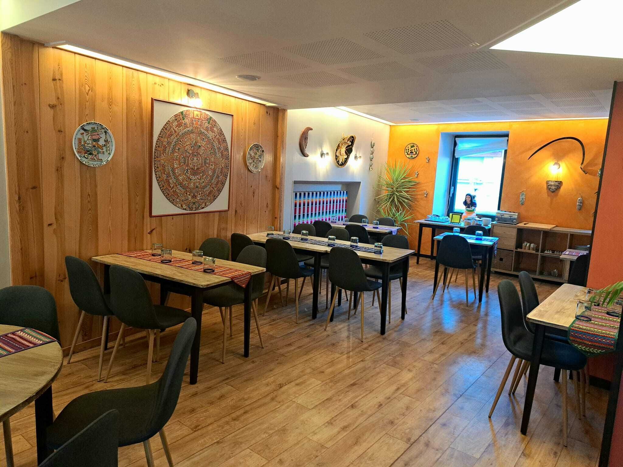 A restaurant with wooden walls, multiple tables, and chairs, and a counter with a person at the end.