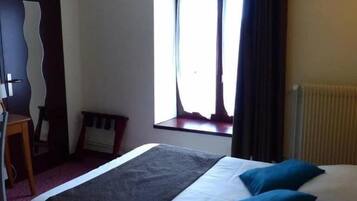 A hotel room with a bed, a chair, a window with curtains, and a radiator.