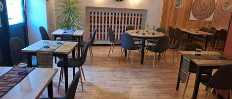 A restaurant with wooden floors, round tables, and black chairs. There are decorative plates on the walls and a potted plant in the center.