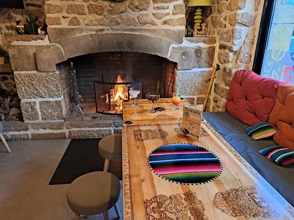 A cozy room with a stone fireplace, a wooden table with a colorful cushion, and a comfortable sofa with pillows.