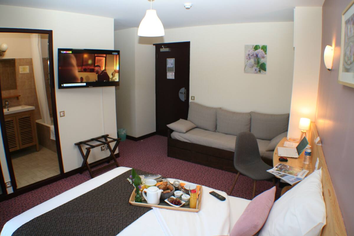 Habitación de hotel con cama, sofá, televisión, bandeja con artículos de desayuno y puerta que da a un baño.