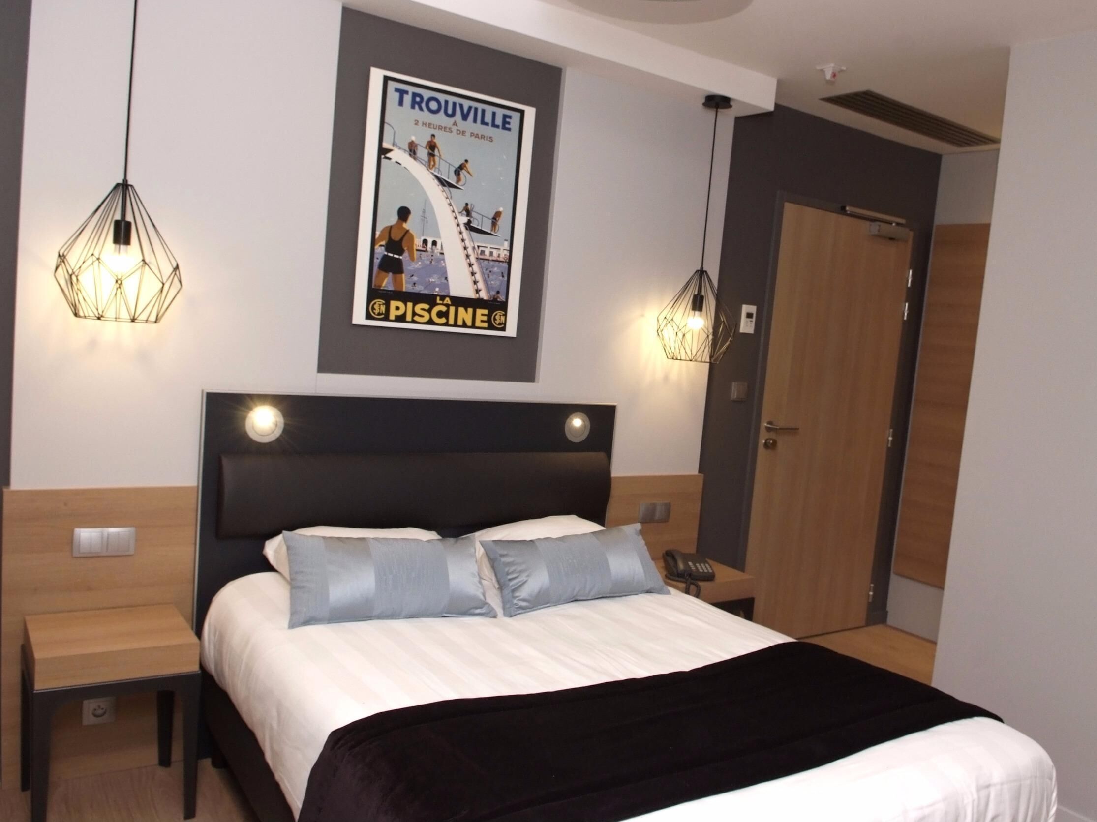 Une chambre d’hôtel avec un lit, des tables de chevet, une affiche au mur et des lampes suspendues.