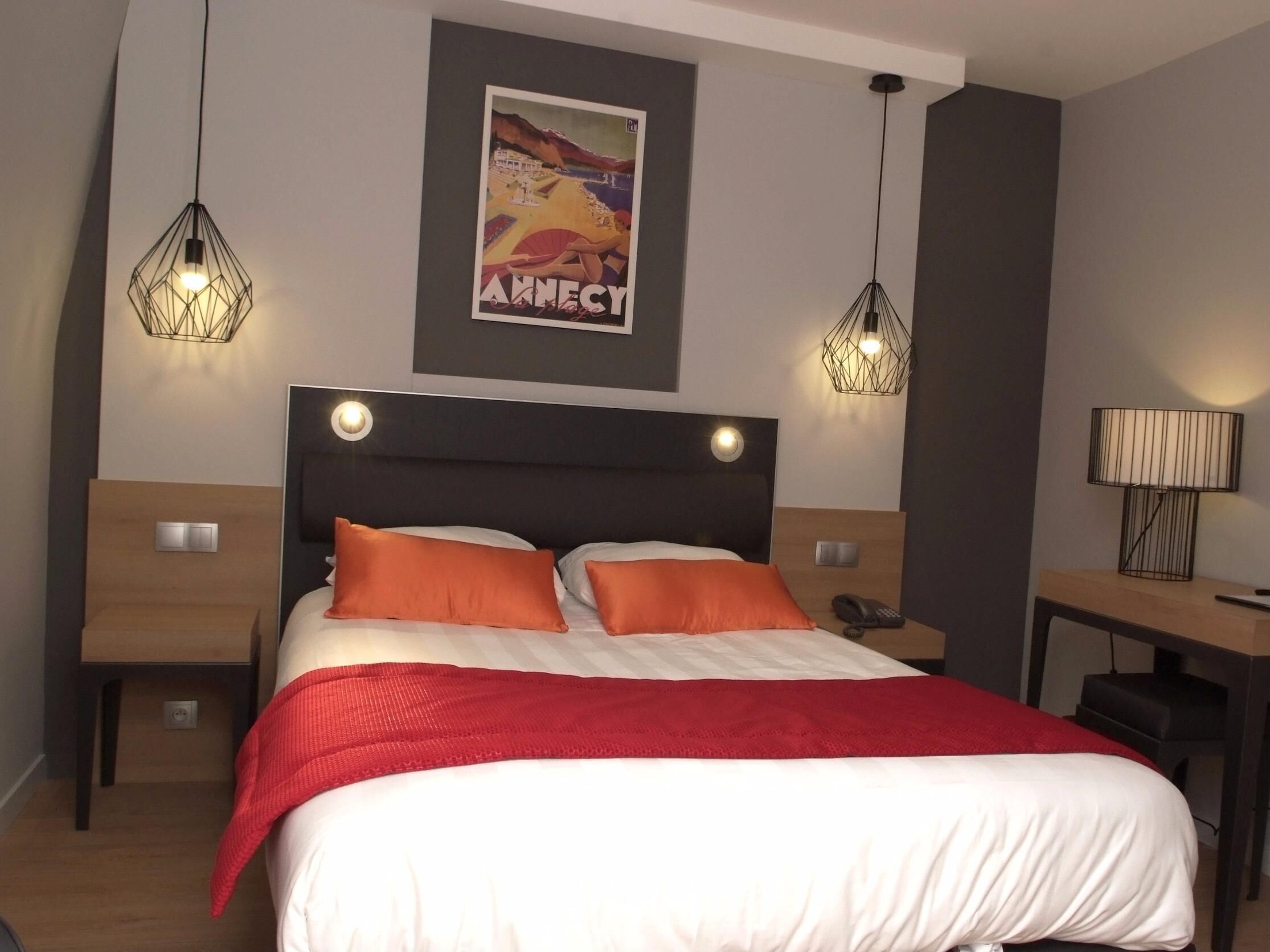 Une chambre d’hôtel moderne avec un grand lit, deux tables de chevet, un bureau et deux lampes suspendues.