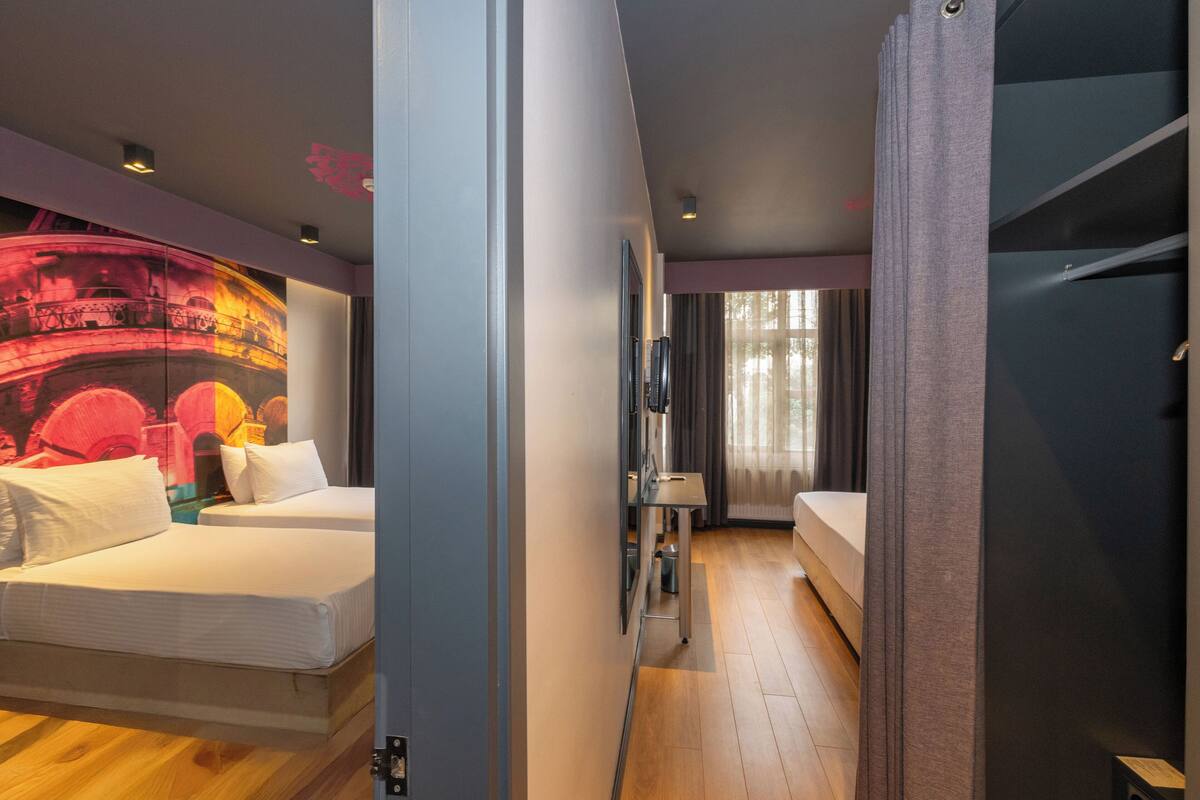 A hotel room with two beds, a small table, and a wall-mounted TV.