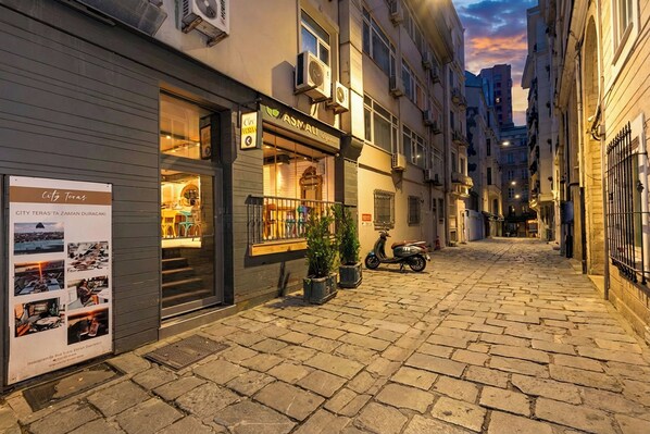 A narrow cobblestone street with a restaurant on the left and a scooter parked nearby.