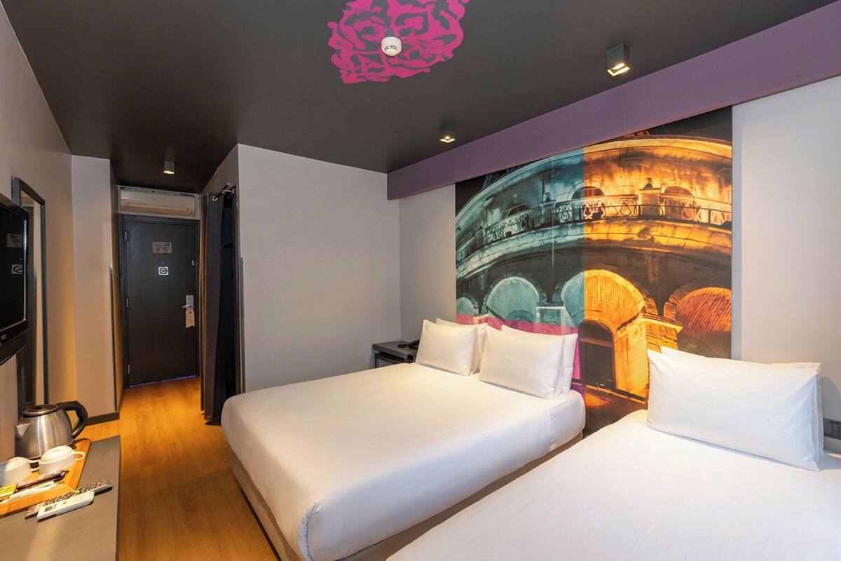 A hotel room with two beds, a flat-screen TV, a coffee maker, and a wall mural of a historical building.