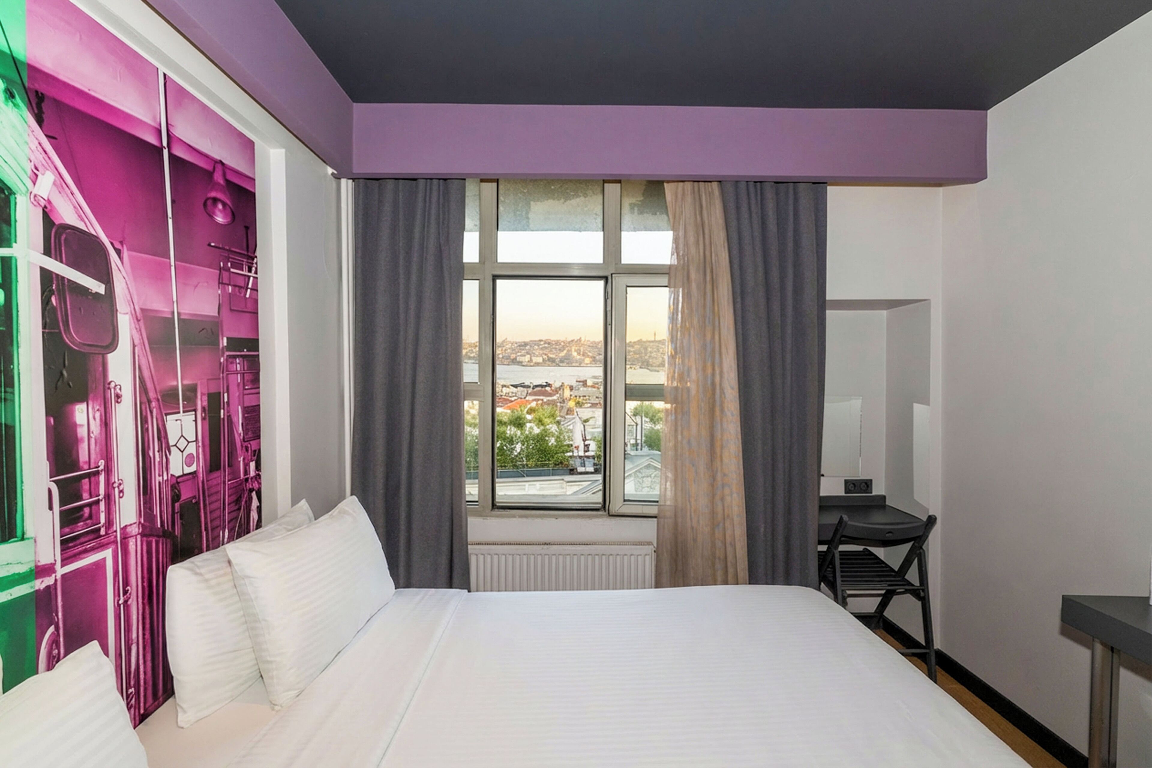 Ein Hotelzimmer mit einem Bett, einem Schreibtisch und einem Fenster mit Blick auf die Stadt.