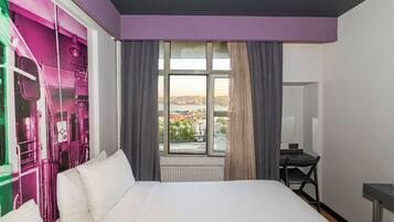 Ein Hotelzimmer mit einem Bett, einem Schreibtisch und einem Fenster mit Blick auf die Stadt.