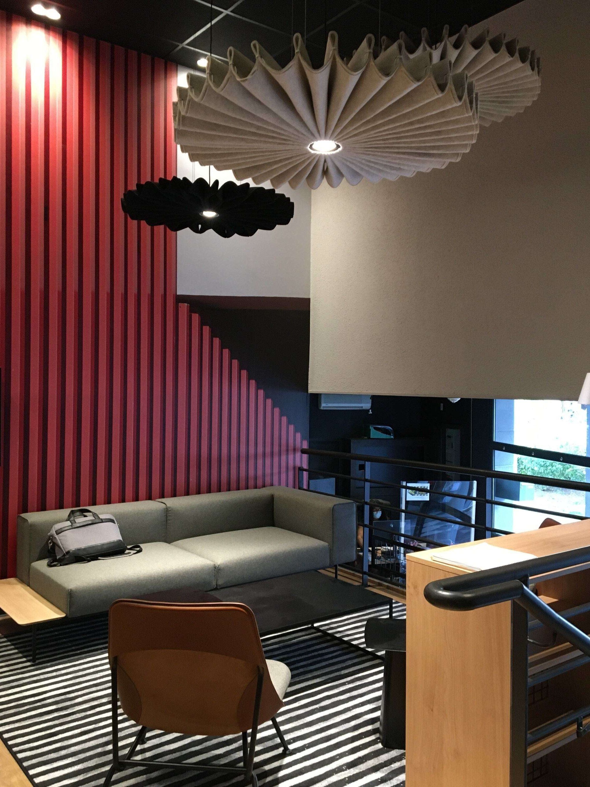 A modern interior with a red striped wall, a grey sofa, a wooden desk, and a unique ceiling light fixture.