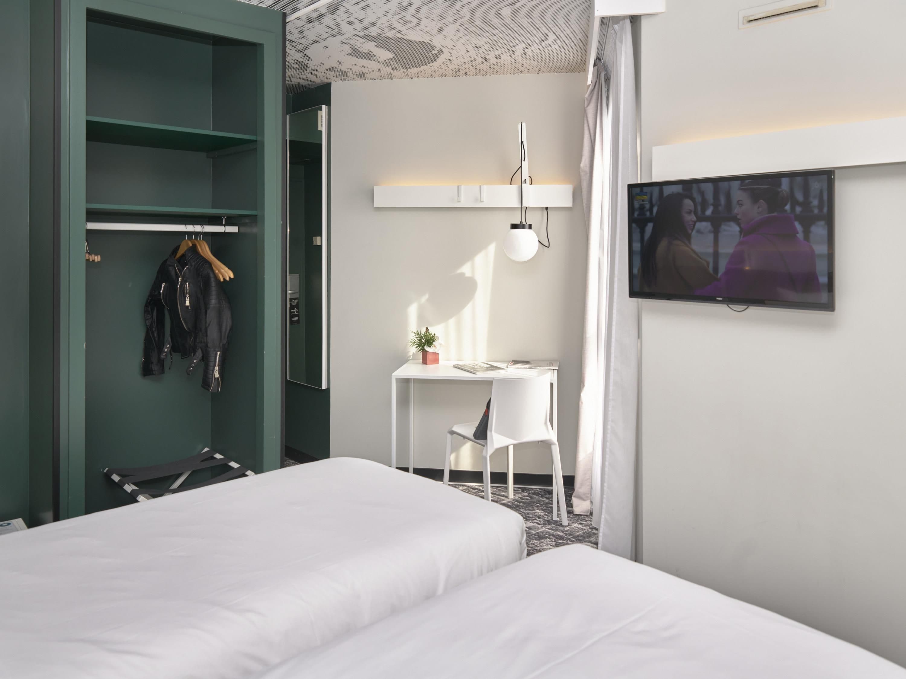 Una habitación de hotel con cama, escritorio, silla, televisor y armario.