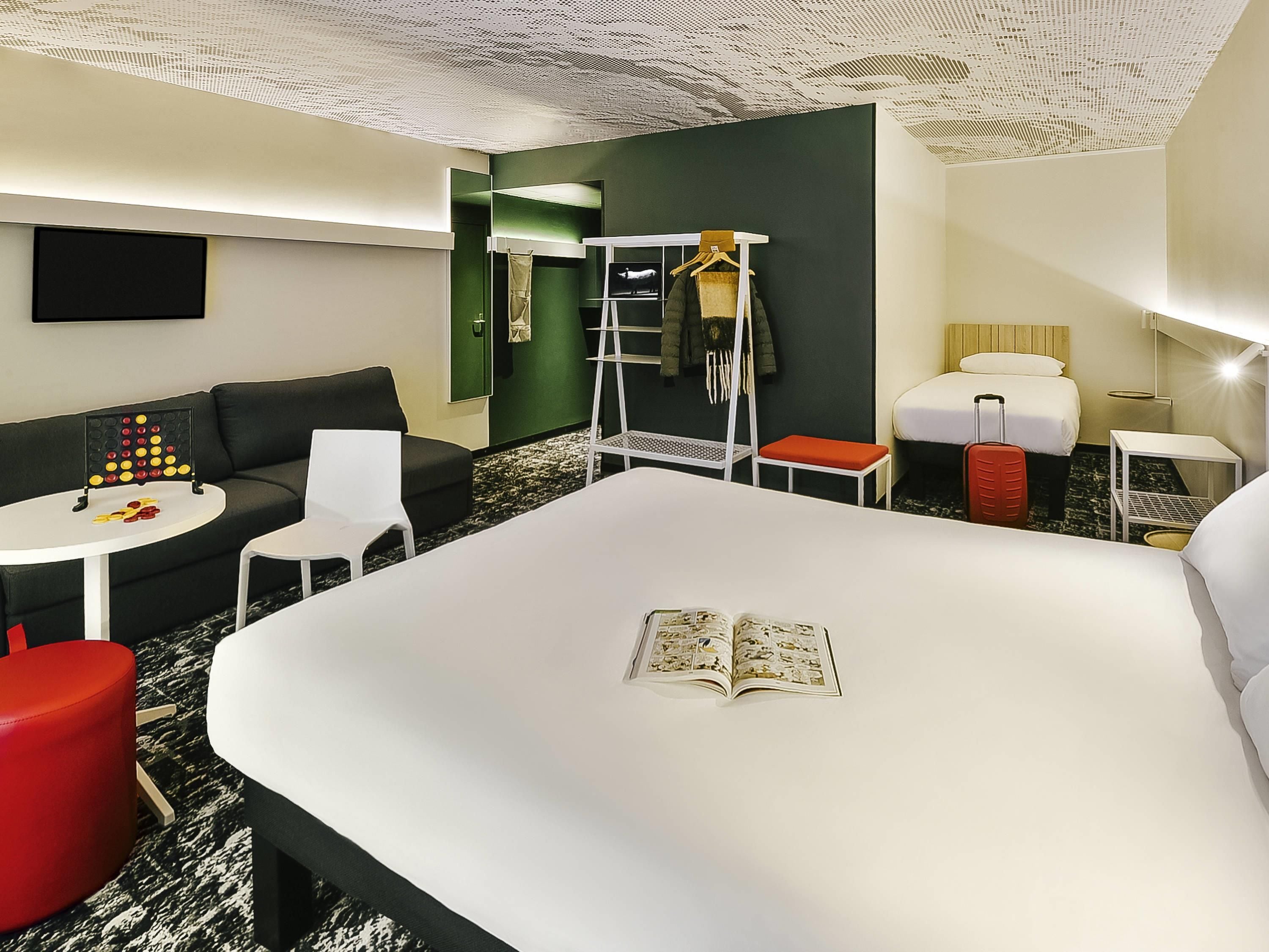 Een hotelkamer met een groot bed, een klein tafeltje, een bank, een rode stoel, een kapstok en een tv aan de muur.