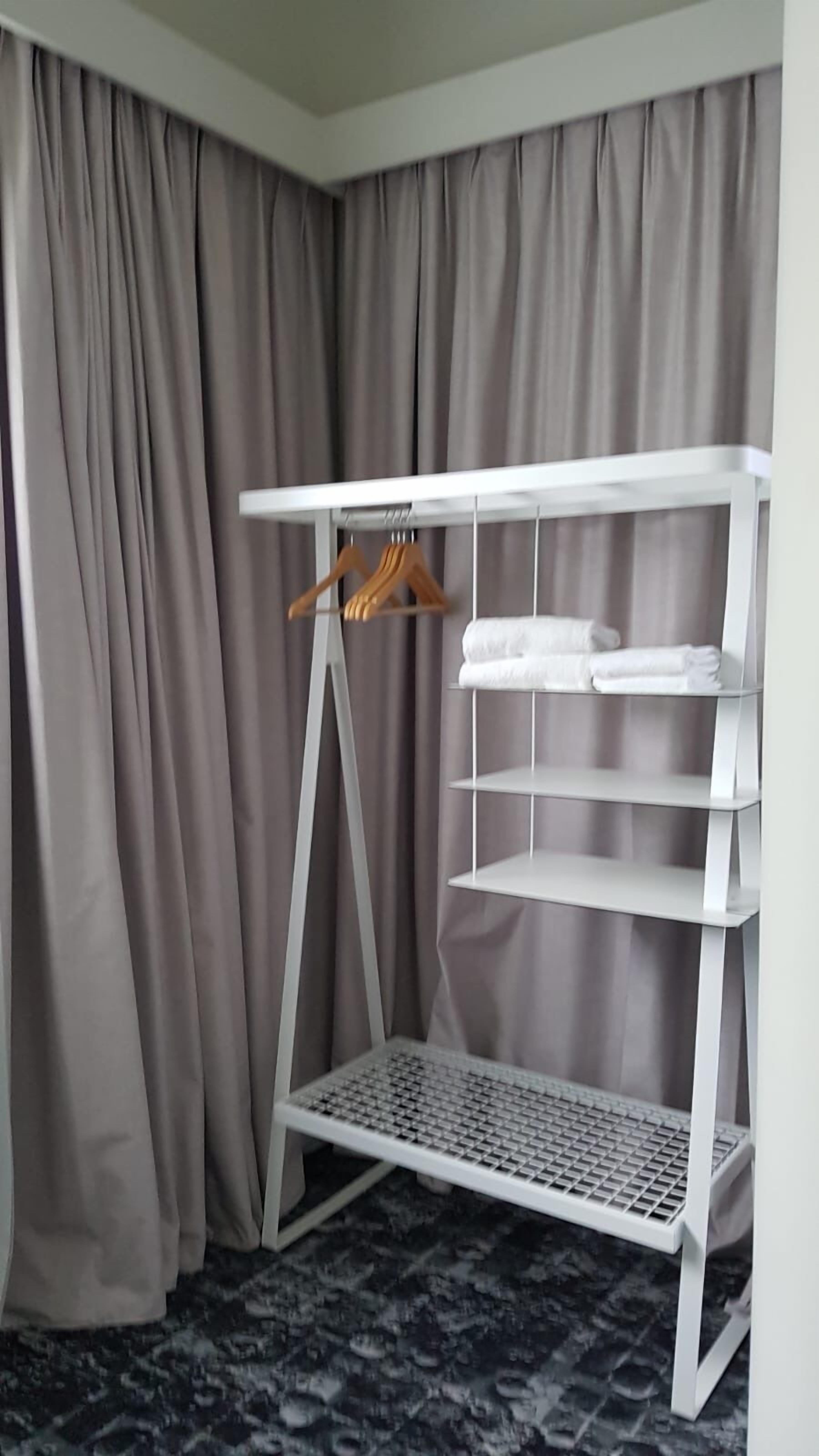 A white metal shelf unit with a hanging rack and shelves, placed against a grey curtain backdrop.