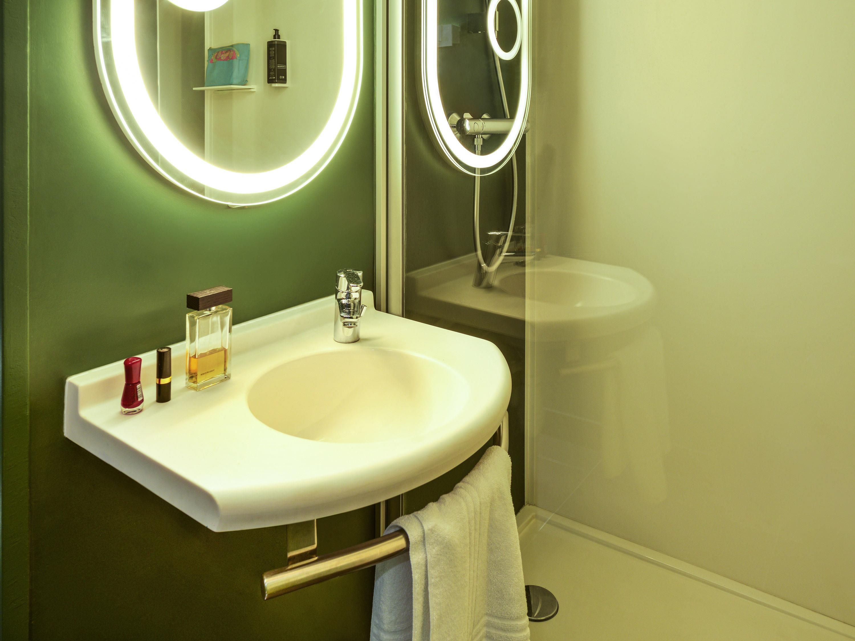 Een badkamer met een witte wastafel, een spiegel met verlichting en een handdoekrek.