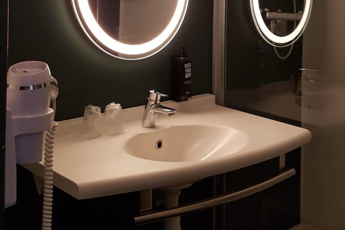 A bathroom with a white sink, a mirror with illuminated edges, and a handheld hairdryer.