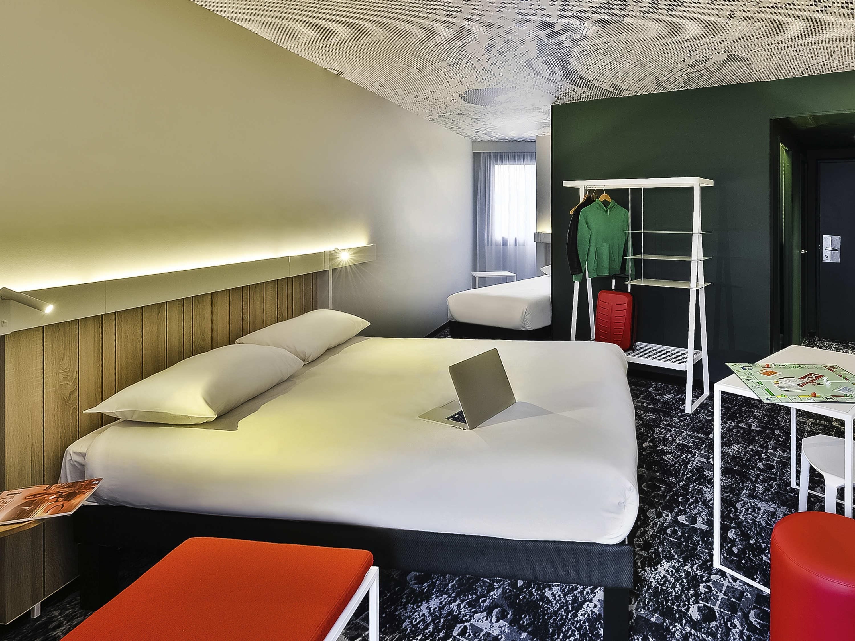 Una habitación de hotel con cama, escritorio, silla, perchero y armario.
