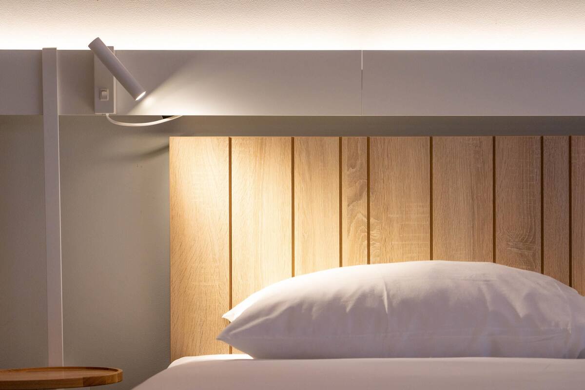 A modern bedroom with a wooden headboard, a bedside table, and a white bedspread.