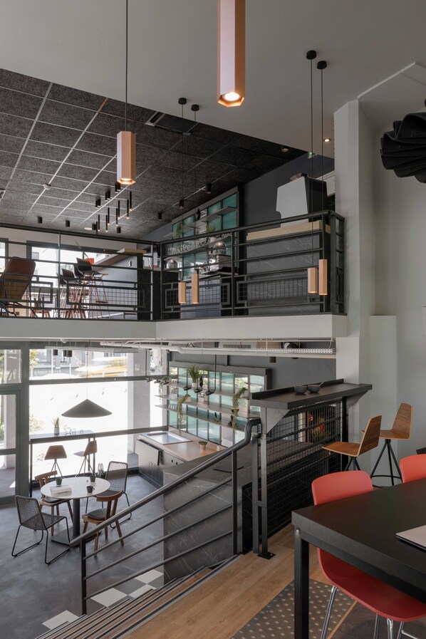 A modern interior with a mezzanine level, open-plan workspace, and a dining area with a staircase. - Ibis Annecy Cran Gevrier Hotel (Annecy)