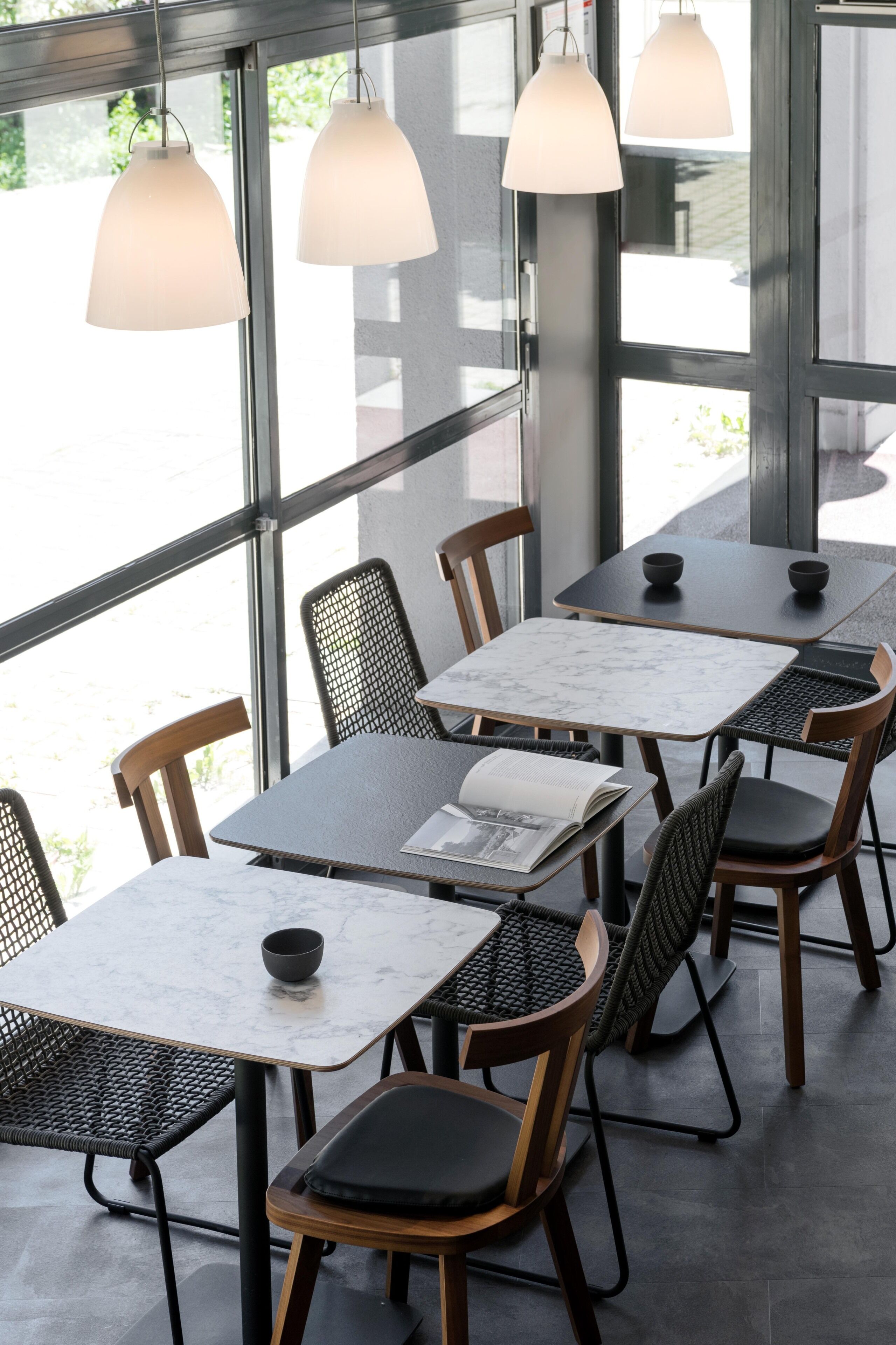 A modern cafe with glass walls, metal chairs, and tables with marble tops.