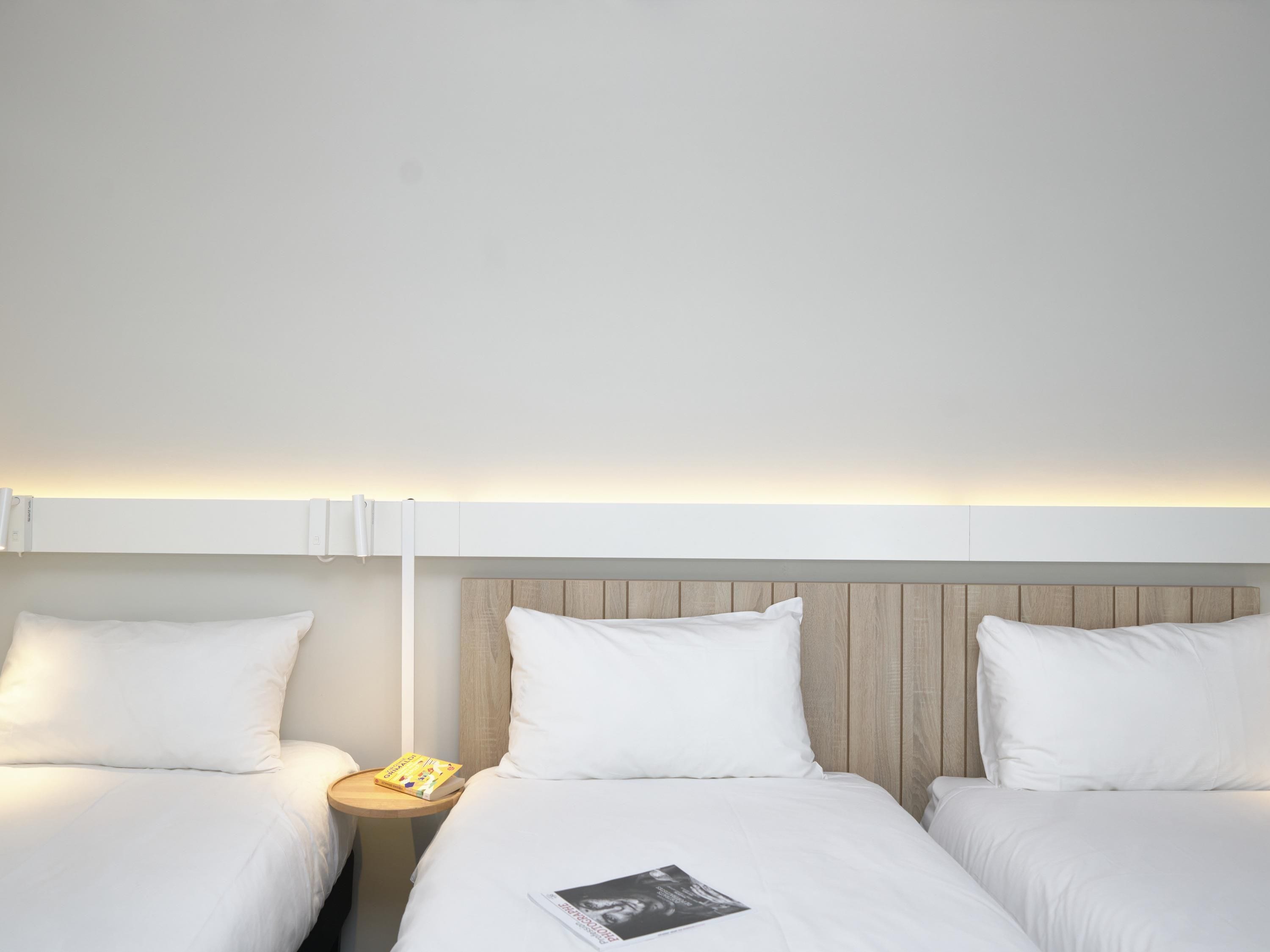Quarto de hotel com duas camas, uma cabeceira de madeira e uma mesa de cabeceira com um livro.