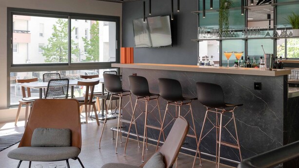 Eine moderne Bar mit einer langen Theke, mehreren Barhocker und einem großen Fenster mit Blick nach draußen.