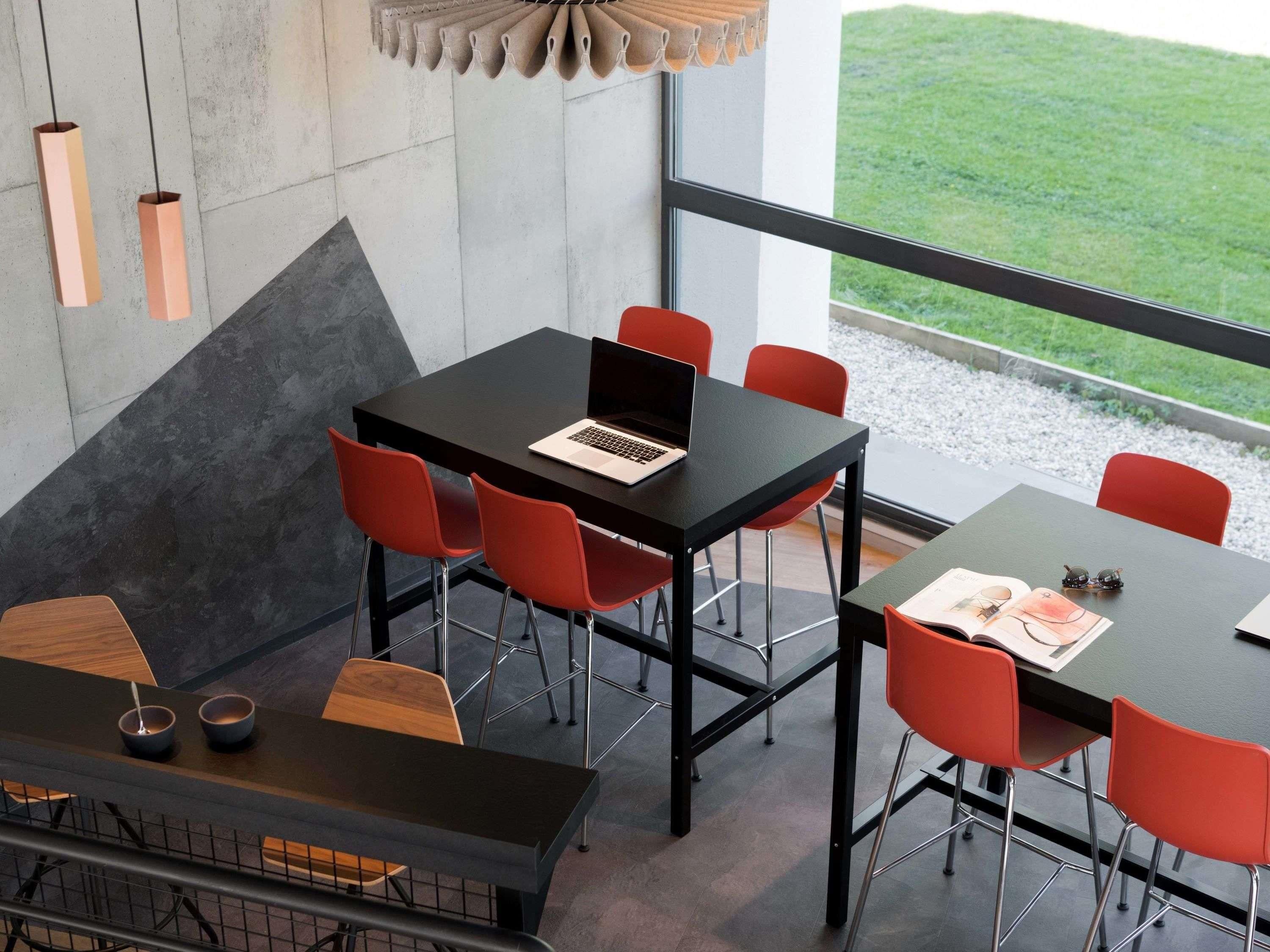 A modern meeting room with a laptop on a table, red chairs, and a view of the outdoors.